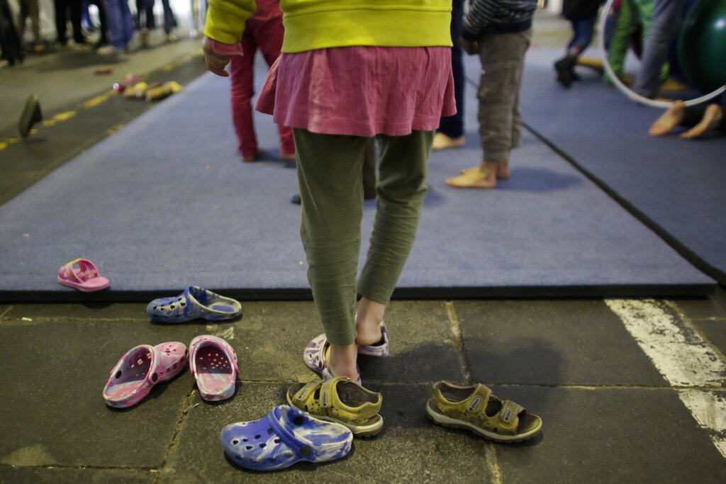 A girl takes of her shoes to attend an artistic program at a temporary emergency shelter for migrants, refugees and asylum seekers inside Hanger 1 of the former airport Tempelhof in Berlin, Wednesday, Dec. 9, 2015.