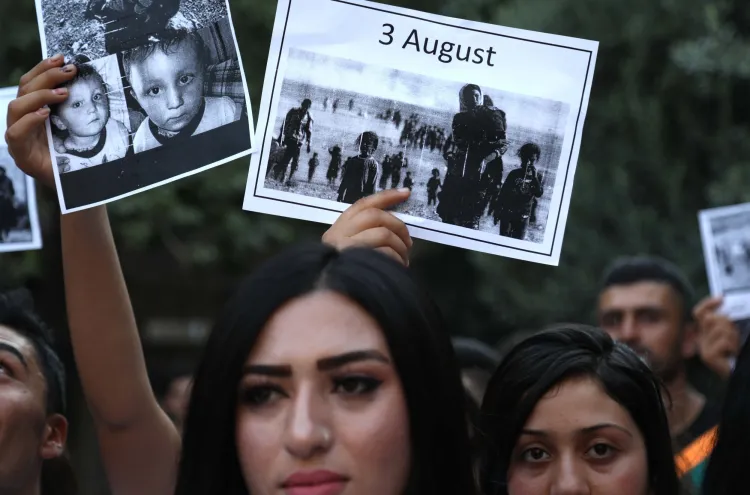 Yazidi women hold signs featuring photos of victims from the 2014 genocide by the Islamic State. Photo: Safin Hamed / AFP via Getty Images  