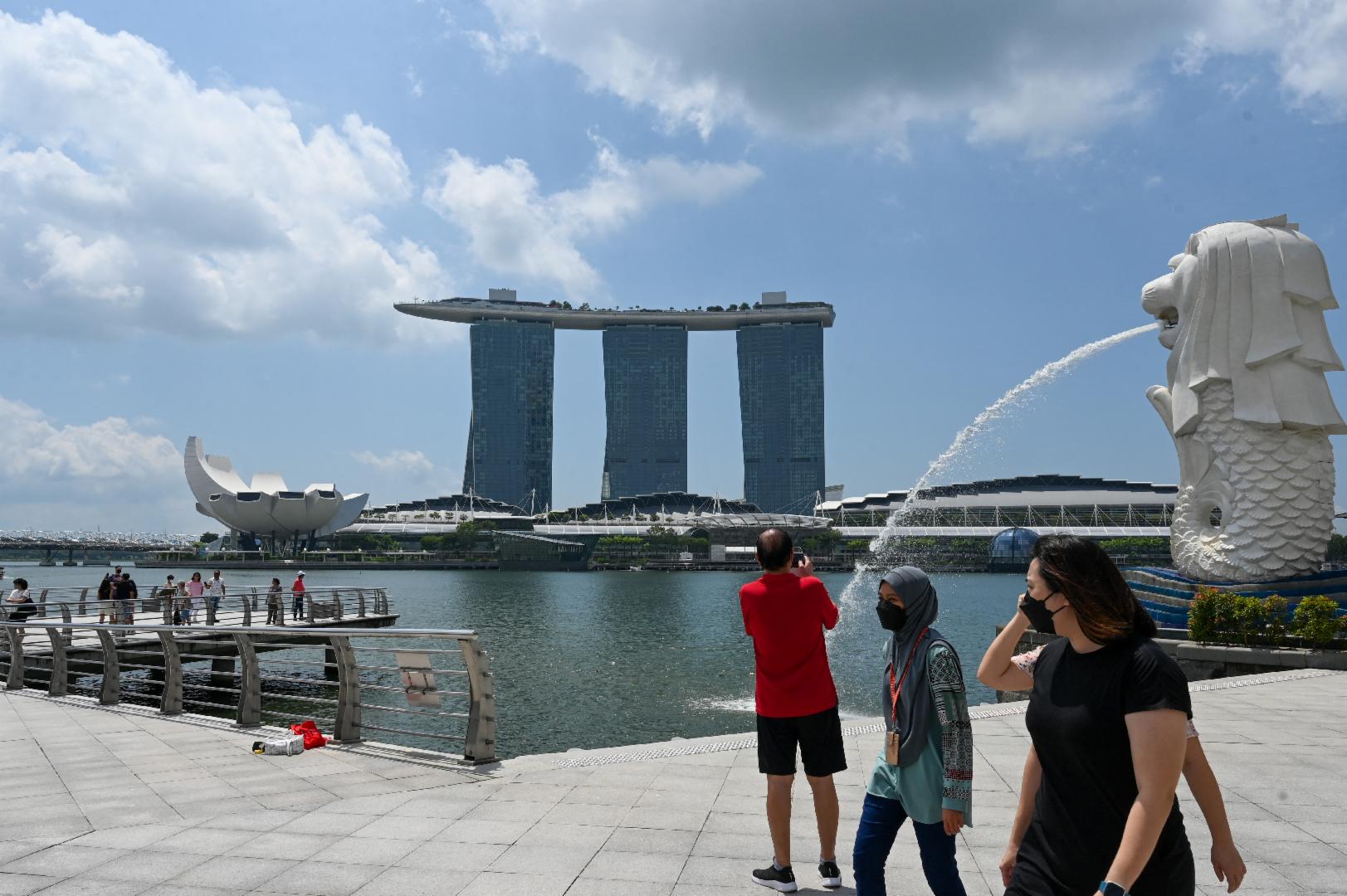 People walk past the Merlion statue in Singapore on March 24, 2022. ( AFP / Roslan Rahman) 
